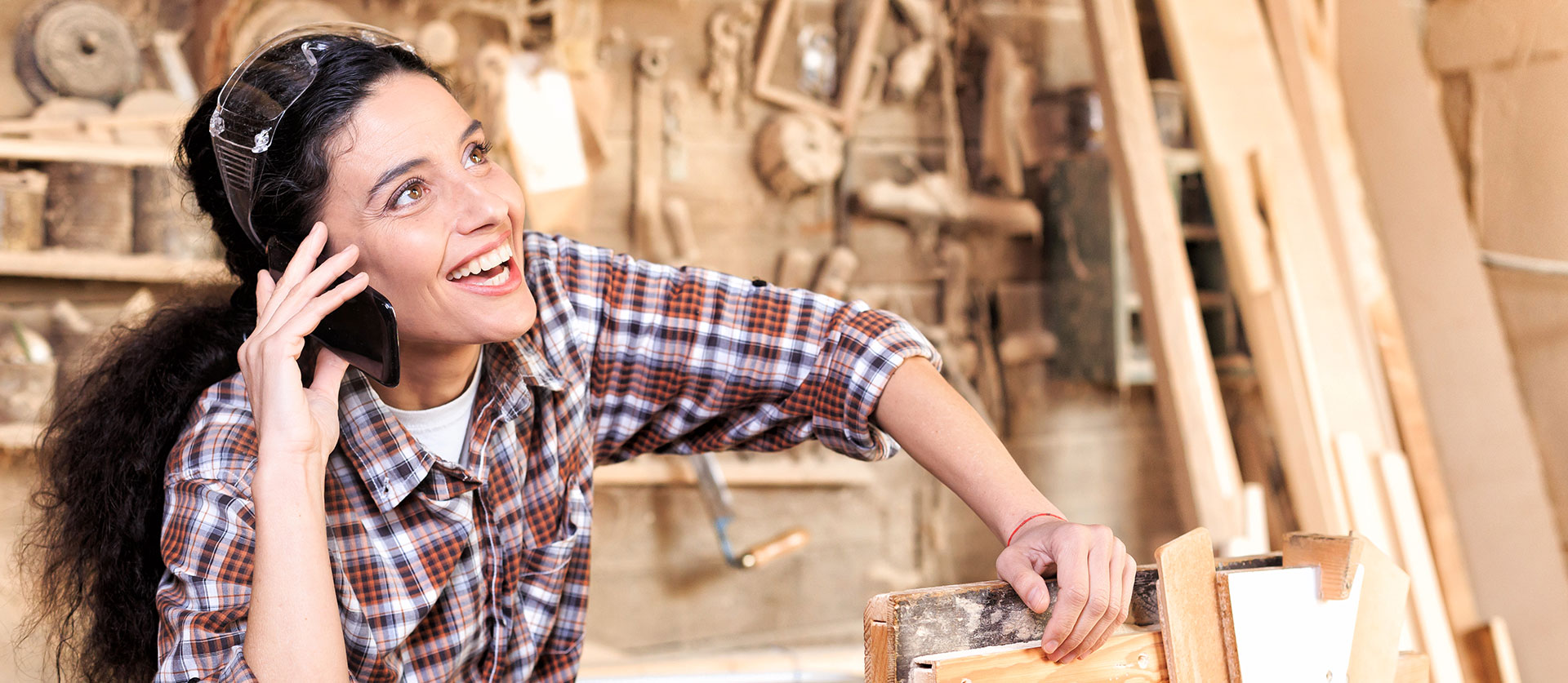 Timmervrouw leunt op houtwerk terwijl ze aan het bellen is met haar mobiele telefoon