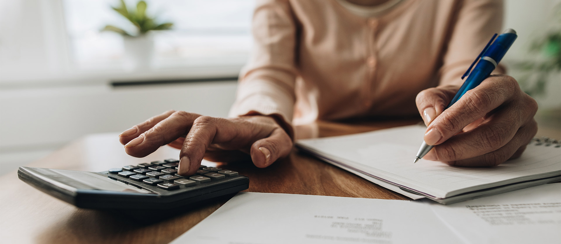 man zit achter een bureau te typen op een rekenmachine en te schrijven met een pen op een kladblok