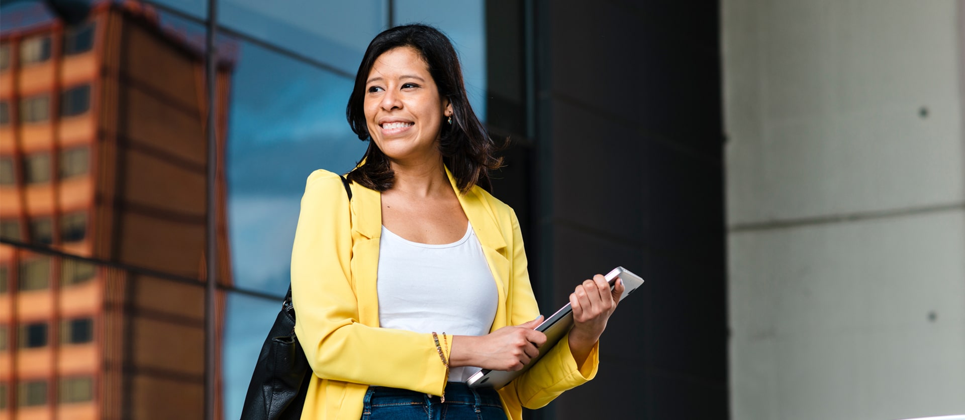 Vrouw staat glimlachend voor een gebouw met een laptop