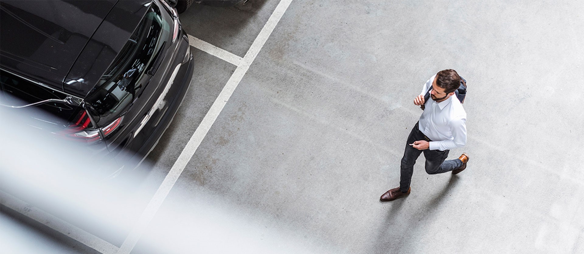 man loopt met rugtas door een parkeergarage met een autosleutel in zijn hand